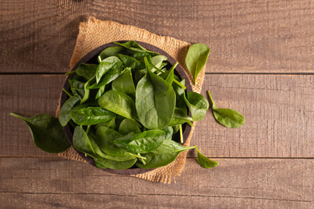 Fresh spinach leaves in bowl on wooden background. Top view, copy space