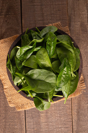 A wooden bowl filled with fresh spinach leaves, placed on a wooden surface.