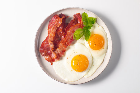 Fried eggs with bacon and basil on a white background, top viewの写真素材