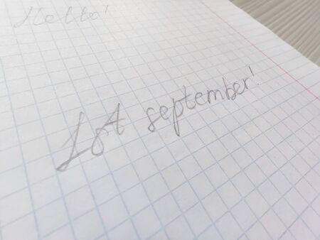 Handwritten inscription in pencil on the first of september on squared paper. Preparation for school, the beginning of the school year, September 1, a sheet in a cage. Hello on the backgroundの写真素材