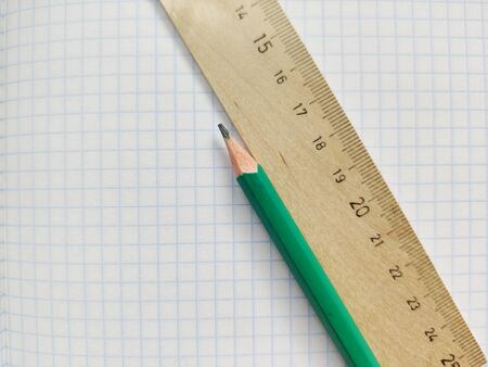 Green pencil and wooden ruler with metric system rests on a white checkered exercise book without notes. School notebook in a cage. Empty notepad with square textureの写真素材