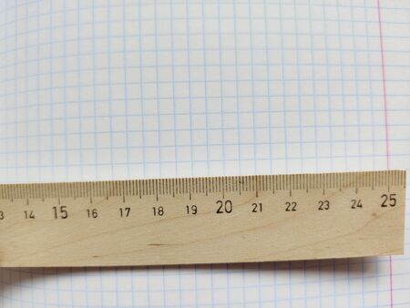 Wooden ruler with metric system rests on a white checkered exercise book without notes. School notebook in a cage. Empty notepad with square texture. Measuring rulerの写真素材