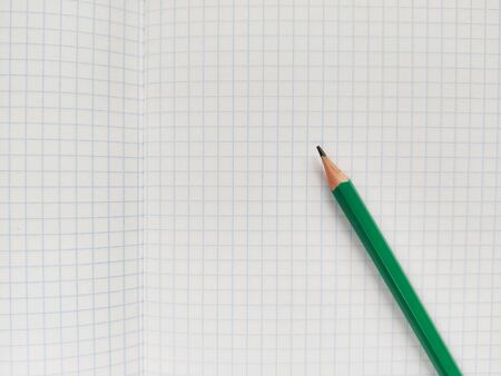 Green pencil rests on a white checkered exercise book without notes. School notebook in a cage. Empty notepad with square textureの写真素材