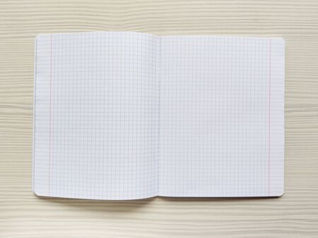 White school notebook in a cage is on a wooden table. Empty notepad is on a desk. Exercise book without notes. Checkered background. Square textureの写真素材