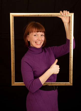a young adult woman holding a frame showing thumb upの写真素材