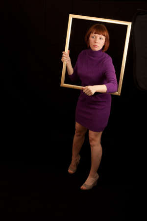 a young adult woman taking a peek through a picture frameの写真素材