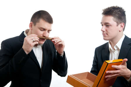 a young businessman smelling the scent of a cigar been offered by anotherの写真素材
