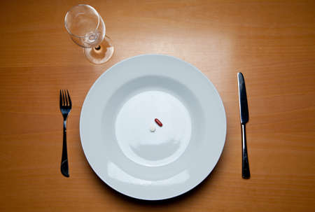 a plate with some pills, cutlery and a wine glass on a wood tableの写真素材