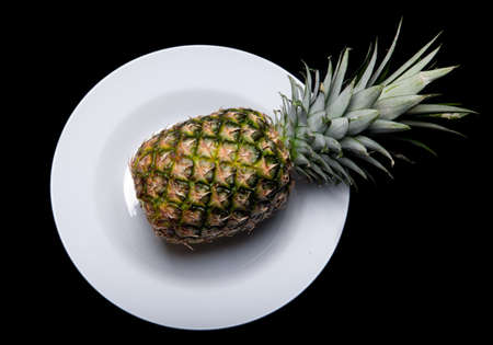 a whole pinapple on a plate isolated on black backgroundの写真素材