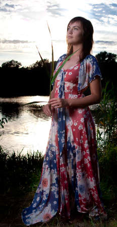 a young woman standing in front of a lake back light from the sun ligthened with flashの写真素材