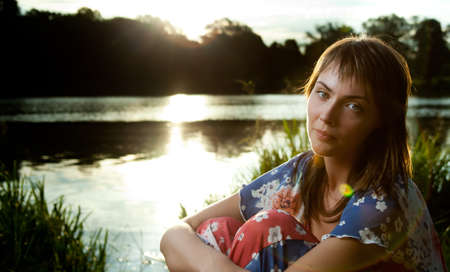 a young woman sitting in front of a lake backlight from the sun lightened up with flashの写真素材