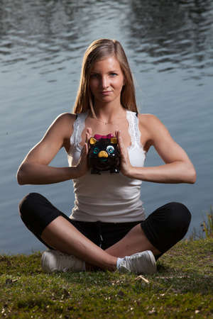 a young woman with a piggy bank meditating in front of a lakeの写真素材