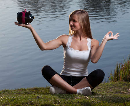 a young woman with a piggy bank meditating in front of a lakeの写真素材
