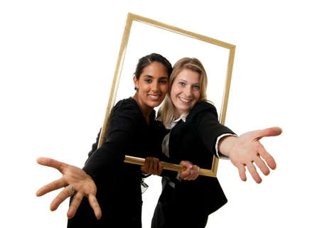 a young indian and a young european businesswoman stretching their hands through a pictureframeの写真素材