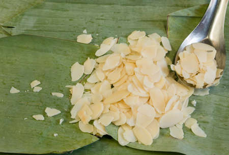 A pile of almond arranged beside the spoon of almonds on the banana leaf backgroundの写真素材