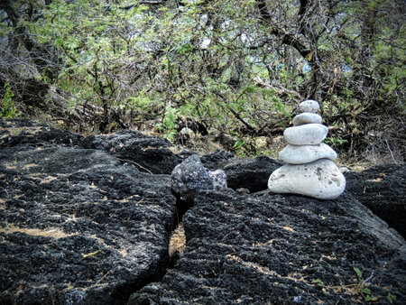 Rock cairn made of white coral sitting on lava rock coast of Maui near Kihei in Ahihi-Kinau Natural Area Reserve Hawaii in zen like peaceful meditation with forest in backgroundの写真素材