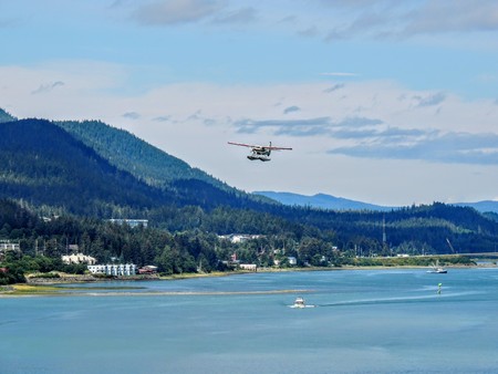 White Float Pontoon Seaplane Taking off from Juneau Harbor with boats and city in backgroundの写真素材