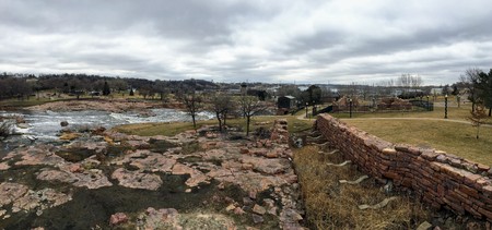 The Big Sioux River flows over rocks in Sioux Falls South Dakota with views of wildlife, ruins, park paths, train track bridge, trees and city in the surrounding area and backgroundの写真素材