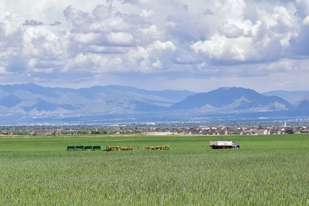 Vintage Farm Truck and harvest machinery with Panoramic view of Wasatch Front Rocky Mountains, Great Salt Lake Valley in early spring with melting snow and Cloudscape. Utah. USA.の写真素材
