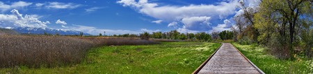 Jordan River Parkway Trail, Redwood Trailhead bordering the Legacy Parkway Trail, panorama views with surrounding trees and silt filled muddy water along the Rocky Mountains, Salt Lake City, Utah.の写真素材