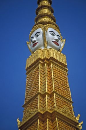 White painted face of Buddha on the golden spire topping the golden roof of the Cambodian Royal Palace in Phnom Penhの写真素材