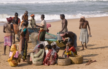 Puri, Orissa, India - May 14, 2008: Fishing boat on a sandy beach in Orissa, India. Fishermen removing the catch from the nets. Women sitting on the ground waiting to take the fish to market.のeditorial素材