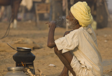 Pushkar, Rajasthan, India -  November 9, 2008: old man smoking next to his camp fire at the annual Pushkar Camel Fair in Rajasthan, Indiaのeditorial素材