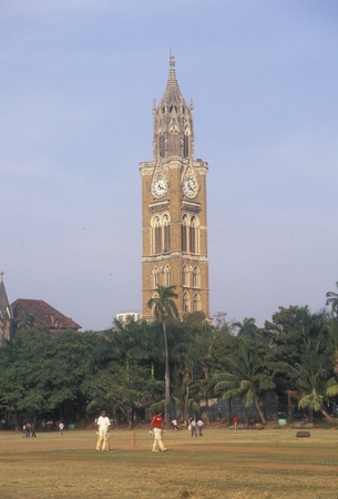 Mumbai, India - November 24, 2006: Large victorian gothic style Rajabai Tower in the centre of Mumbai. Cricket match being played in the park in front.のeditorial素材