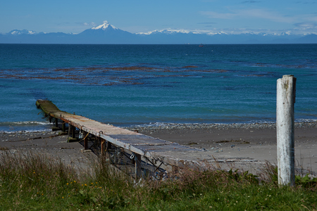 Jetty jutting out into the sea from the Island of Chiloe towards the snow capped mountains and the Corcovado Volcano on the mainland of Chile.の写真素材