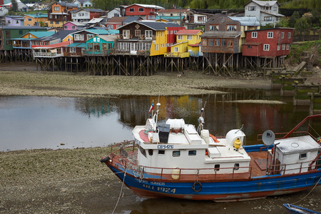 CASTRO, CHILE - OCTOBER 15, 2015: Fishing boat resting on the mud at low tide next to a row of houses built on stilts, known locally as Palafitos in Castro, capital of the Island of Chiloe.のeditorial素材
