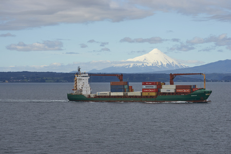 Puerto Montt, Chile - November 22, 2017: Container ship heading south along the coast of Chile from Puerto Montt. Snow capped peak of Volcano Osorno in the background.のeditorial素材