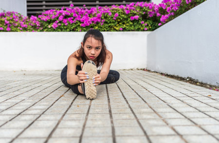 One asian young woman with black long hair in black sports attire active workout stretching thigh legs at outdoorの写真素材
