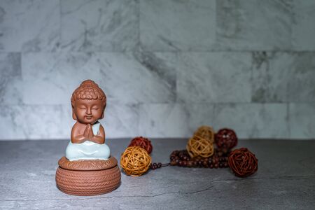 Monk sitting down praying statue home decoration ornament in spotlight casting shadow. Rattan cane balls, praying beads. Empty copy space for text. Marble texture background.の写真素材