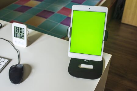 Work from home, mobile tablet, mouse, and LED clock with green screen on desktopの写真素材