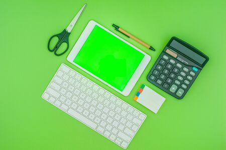 Green screen tablet, keyboard, office school stationery on green background. Flat lay top down view. Business Objects Technology concept.の写真素材