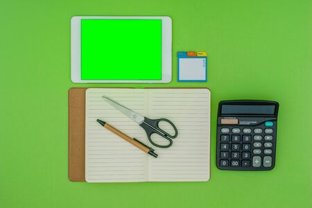 Green screen tablet, office school stationery on green background. Flat lay top down view. Business Objects Technology concept.の写真素材