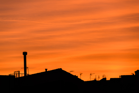 Red sky sunset with clouds, roofs, antennas and planeの写真素材