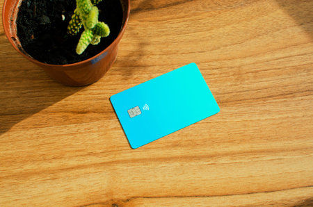 Plastic credit card with chip visible, on top of a table with soft lights and shadows. Blue card on...