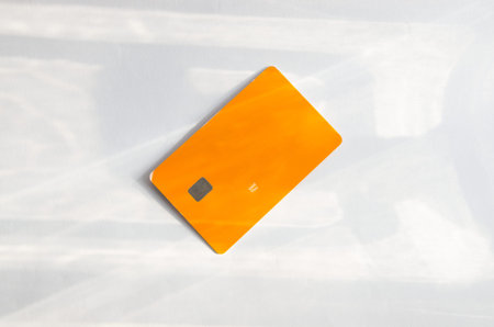 Plastic credit card with chip visible, on top of a table with soft lights and shadows. Orange color...