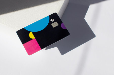 Plastic credit card with chip visible, on top of a table with soft lights and shadows. Colored card on white surface. Concept: finance, purchases, payments, loan, spending, investments and debts.の写真素材