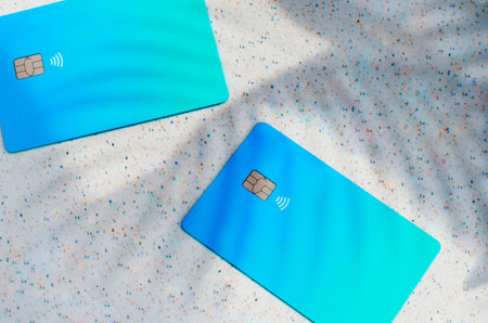 Plastic credit card with chip visible, on top of a table with soft lights and shadows. Blue card on white surface. Concept: finance, purchases, payments, loan, spending, investments and debts.の写真素材