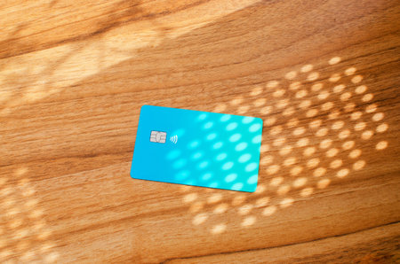 Plastic credit card with chip visible, on top of a table with soft lights and shadows. Blue card on...