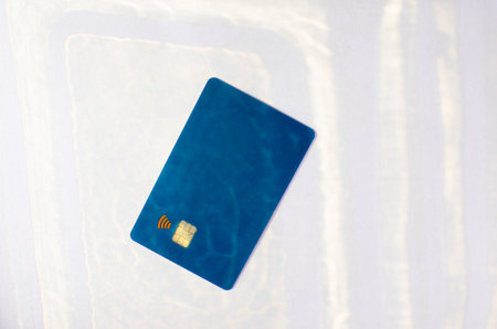 Plastic credit card with chip visible, on top of a table with soft lights and shadows. Blue card on white surface. Concept: finance, purchases, payments, loan, spending, investments and debts.の写真素材