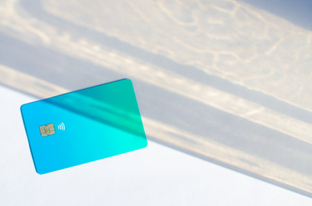 Plastic credit card with chip visible, on top of a table with soft lights and shadows. Blue card on white surface. Concept: finance, purchases, payments, loan, spending, investments and debts.の写真素材
