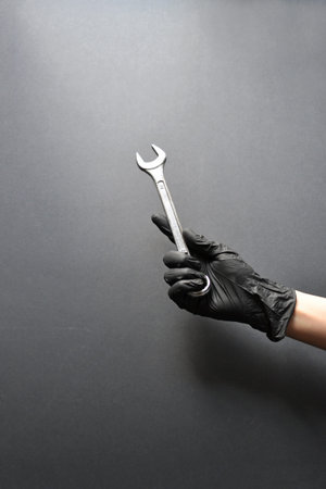 Wrench in a female hand in a glove on a black background. Repair, plumbing work