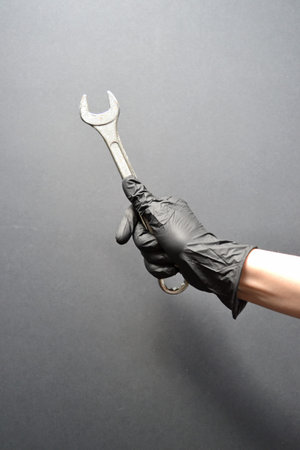 Wrench in a female hand in a glove on a black background. Repair, plumbing work