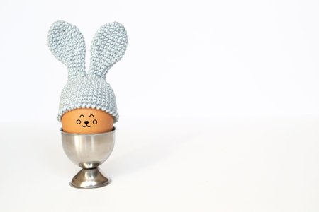 Easter egg in crochet cap with bunny ears in an egg holder with copy space on a white background....