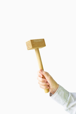 Wooden hammer for meat in a female hand on a white background