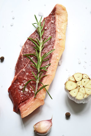 Fresh and raw beef meat. A whole piece of tenderloin with rosemary and pepper ready to cook on a white backgroundの写真素材