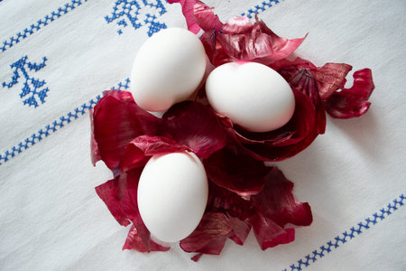 White chicken eggs in red onion husks on a white embroidered tablecloth.